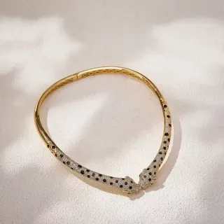 Pulsera de brazalete dorada con pavé de piedras negras y transparentes y cabeza de animal